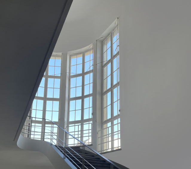 Here you can see a staircase in a house. There are three high windows there. The blue sky is behind them.