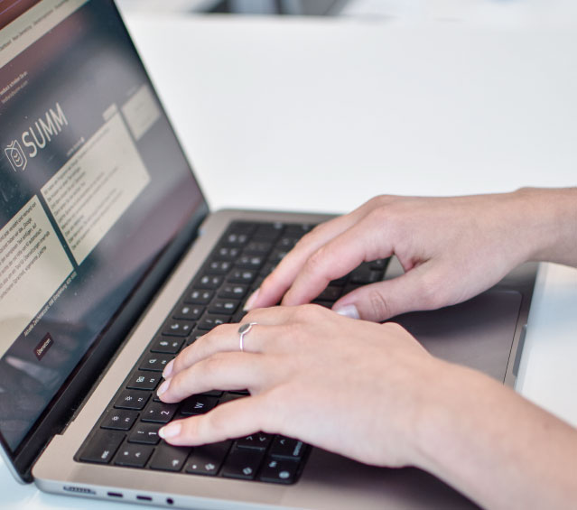 Zwei Hände tippen an einem Laptop. Auf dem Bildschirm sind die Internetseite von SUMM und das Übersetzungstool zu sehen.