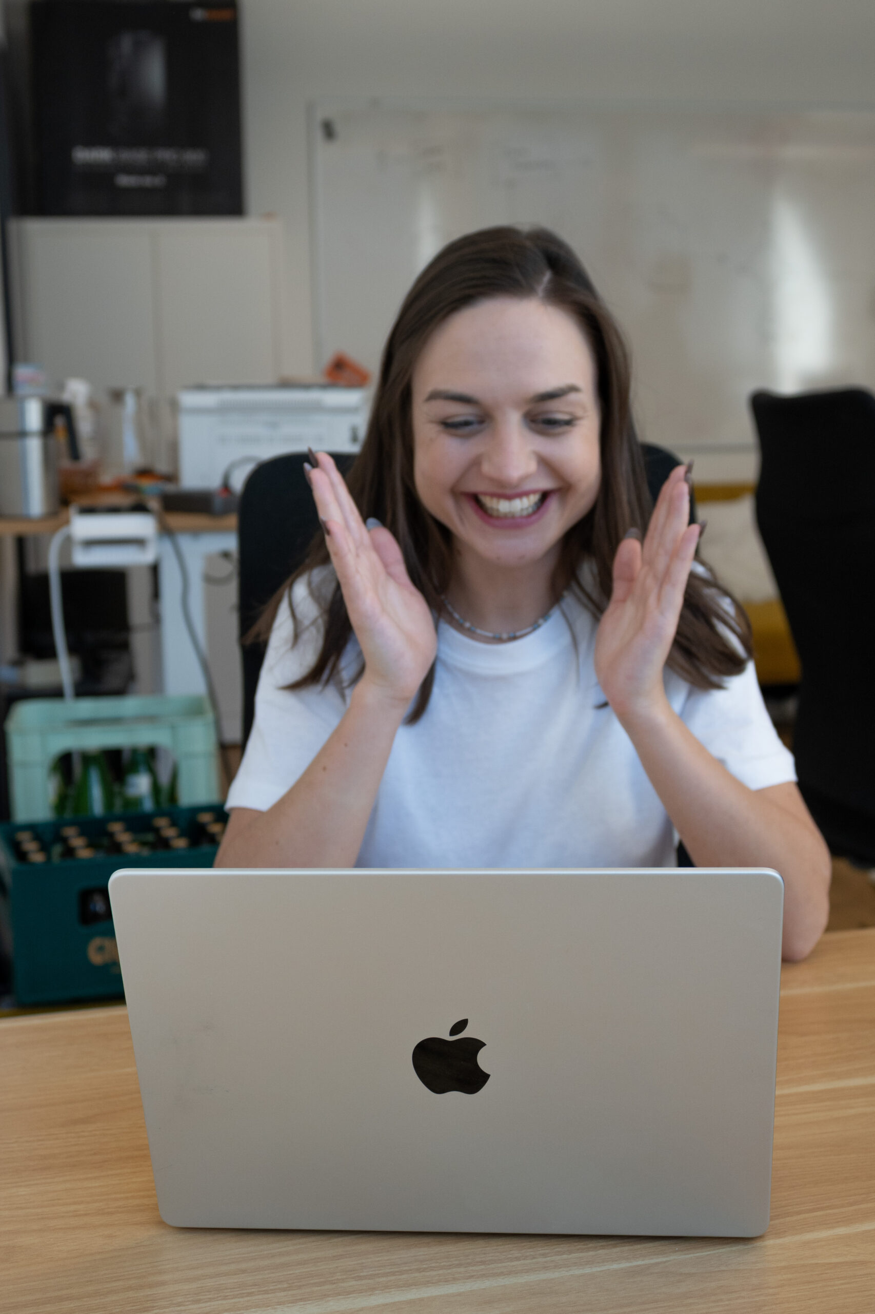 Eine Mitarbeiterin von SUMM AI sitzt in den Büroräumen der Firma mit einem breiten Lachen im Gesicht vor einem aufgeklappten Laptop und hebt ihre Hände erfreut in die Höhe.