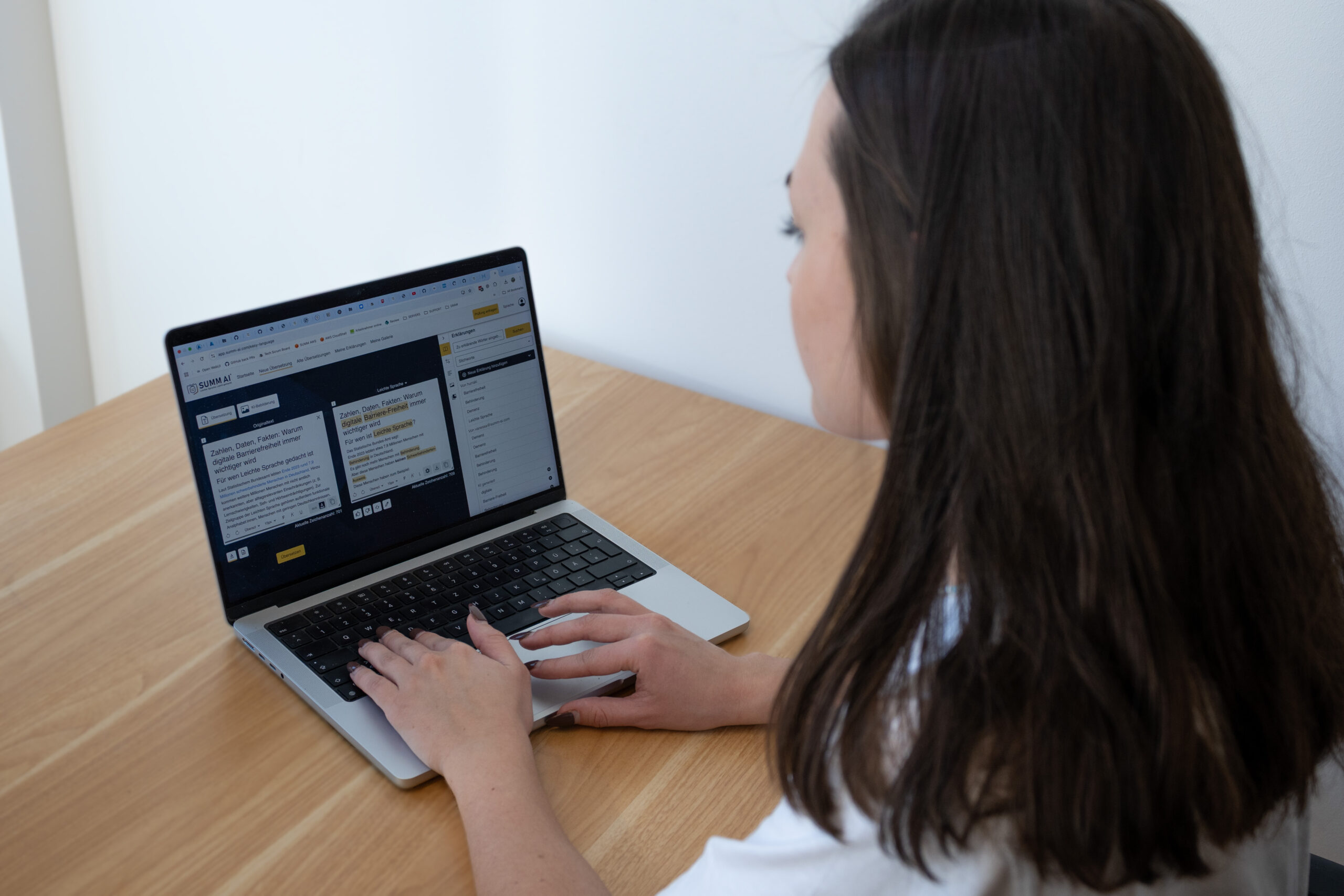 leichte-sprache-wichtig-zielgruppe-pruefgruppe-erklaerung Zwei Menschen sitzen an einem Tisch. Auf dem Tisch ist ein Laptop. Ein Mensch tippt auf dem Laptop etwas ein. Der Laptop zeigt die Webseite von SUMM und das Übersetzungstool. Wir blicken hier von hinten wie die zwei Menschen auf den Laptop.
