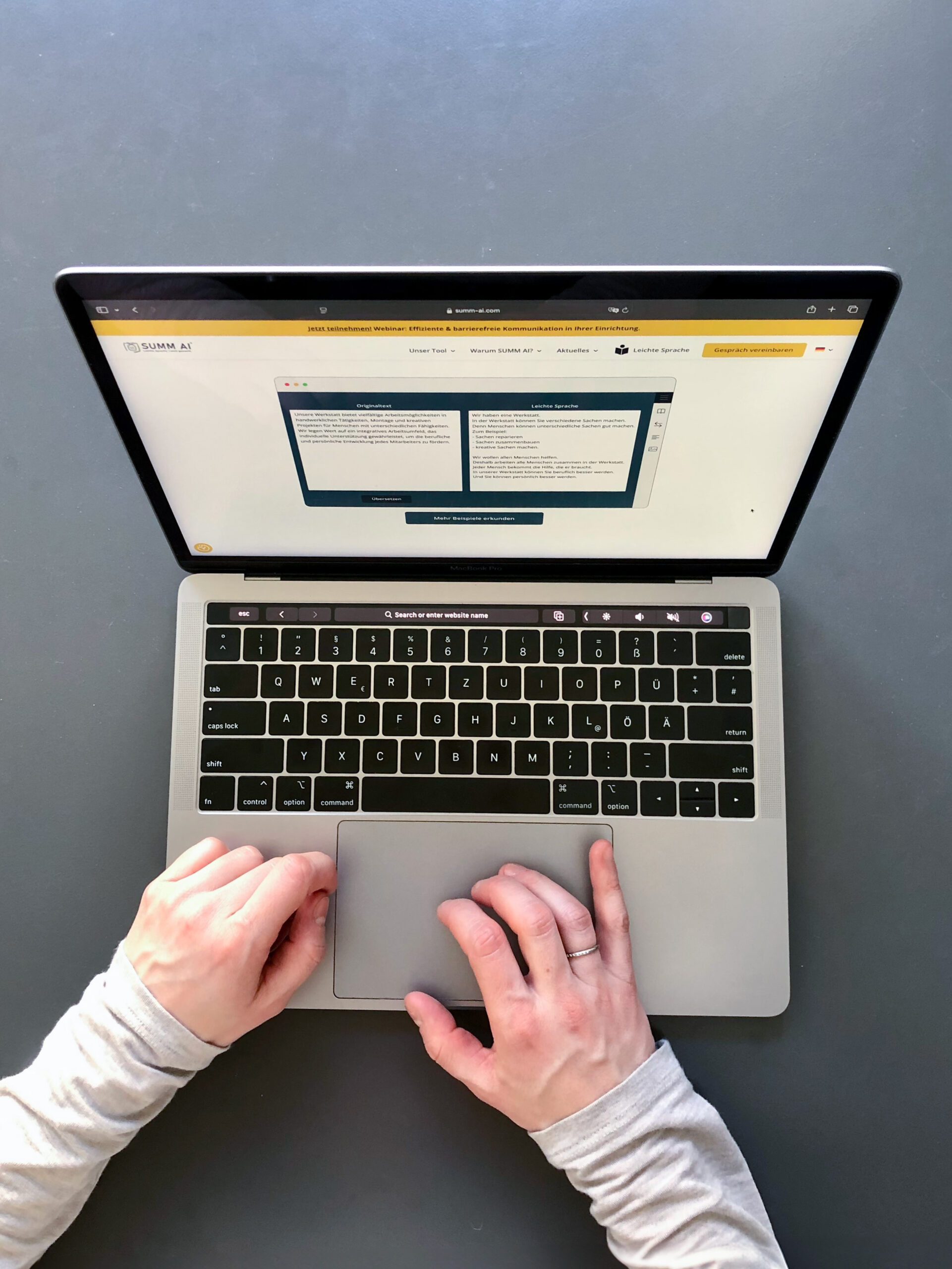 Eine Mitarbeiterin von SUMM AI sitzt in den Büroräumen der Firma mit einem breiten Lachen im Gesicht vor einem aufgeklappten Laptop und hebt ihre Hände erfreut in die Höhe.